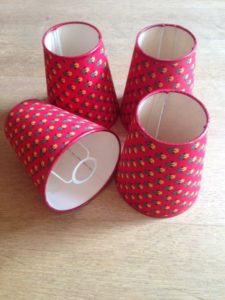 Quatre petits abat-jour rouges rétro avec un motif jaune et noir, disposés sur une surface en bois, évoquent une charmante ambiance 93 brocante.