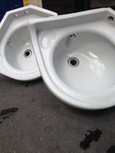 Deux éviers vintage en céramique blanche posés au sol, légèrement superposés, avec drains visibles et surface en béton en dessous.