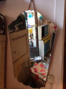 Miroir asymétrique réfléchissant accroché au mur, montrant une pièce avec divers objets vintage et colorés, dégageant une ambiance rétro Brocante.