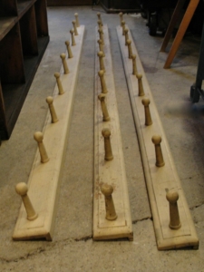 Trois longs porte-manteaux en bois avec patères, au charme vintage, exposés sur un sol en béton.