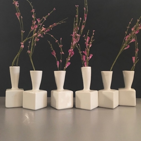 Six vases tubes soliflores en porcelaine avec de simples fleurs roses sur un fond sombre, mettant en valeur l'élégance et le charme des trésors de brocante. Brocante 93