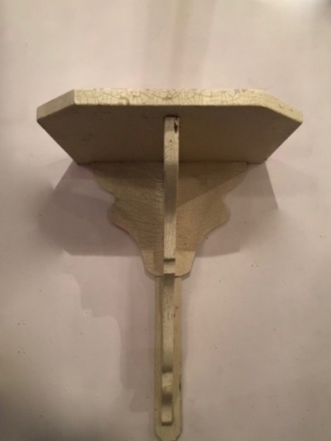 Un petit support d'étagère murale décoratif en forme de piédestal pour statue des années 1930, avec une finition de peinture craquelée de couleur crème et un charme brocante, monté contre un mur uni. Brocante 93