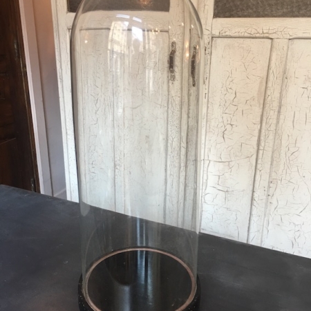 Le Globe de Mariage XL 1930, un grand dôme en verre transparent avec une base noire, se dresse gracieusement sur une surface sombre, évoquant le charme de la brocante devant un mur blanc texturé. Brocante 93