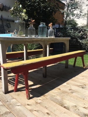 Une table en bois avec des vases à fleurs et un Bancs de Salle des Fêtes 1960 sur une terrasse extérieure ensoleillée créent une charmante ambiance brocante 93. Brocante 93