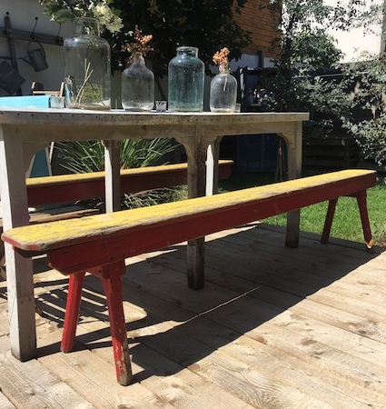 Une table en bois avec des vases à fleurs et un Bancs de Salle des Fêtes 1960 sur une terrasse extérieure ensoleillée créent une charmante ambiance brocante 93. Brocante 93