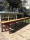 Une table en bois avec des vases à fleurs et un Bancs de Salle des Fêtes 1960 sur une terrasse extérieure ensoleillée créent une charmante ambiance brocante 93. Brocante 93