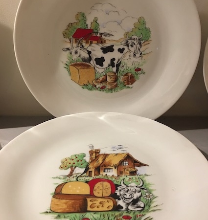 Deux assiettes décoratives de la collection « Assiettes à Fromage 1970 », l'une ornée d'une vache et l'autre d'une maison, de fromages, de moutons et de champignons. De belles trouvailles chez Brocante 93. Brocante 93