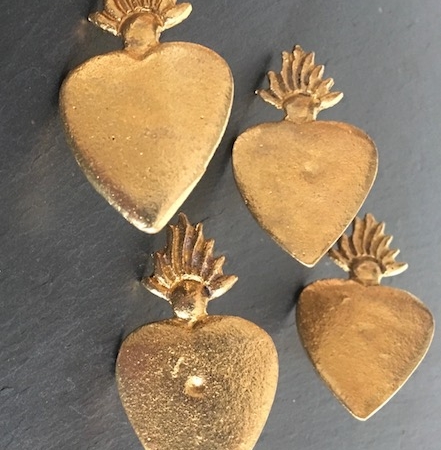 Trois pendentifs en forme de cœur en or Clou Coeur avec des motifs en forme de flamme sur le dessus, astucieusement disposés sur une surface sombre, évoquent l'attrait de la brocante 93. Brocante 93