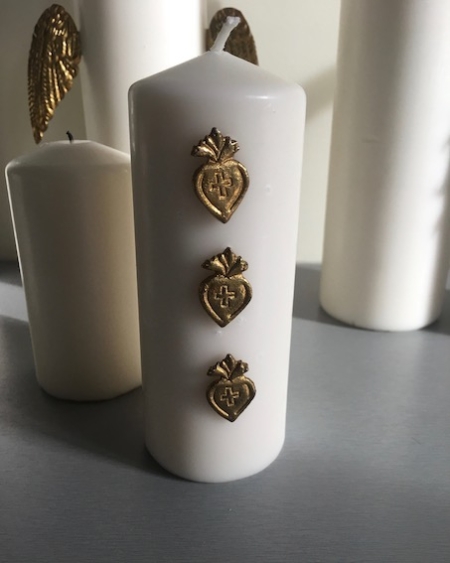 La bougie Bijoux de Bougies Coeurs arbore un extérieur blanc orné de trois symboles de cœur dorés alignés verticalement, évoquant le charme des trésors de brocante, et est représentée parmi d'autres élégantes bougies blanches. Brocante 93