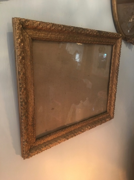 Un cadre Cadre Moulé 1930 VENDU vide, orné de détails dorés complexes, est accroché sur un mur beige, dégageant un charme vintage rappelant les trouvailles de brocante 93. Brocante 93
