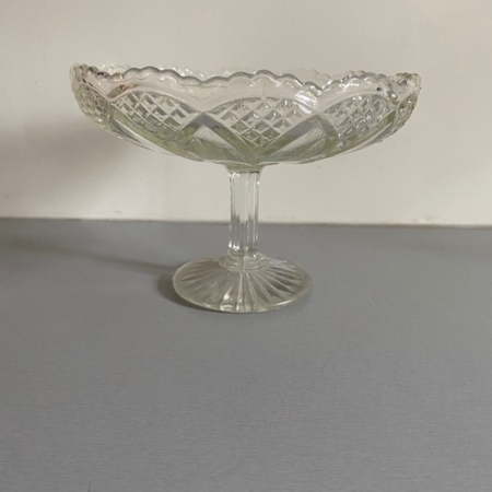 La Coupe en Verre 1950 Motifs Feuilles est un bol sur pied en verre transparent présentant un bord festonné et un motif de feuilles complexe, dégageant un charme rétro sur une surface unie. Brocante 93