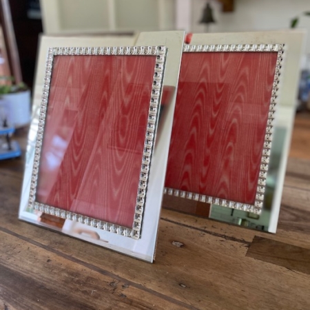 Deux cadres photo vintage Cadre Miroir 1950 en argent avec des accents de cristal et un fond rouge, placés sur une surface en bois. Brocante 93