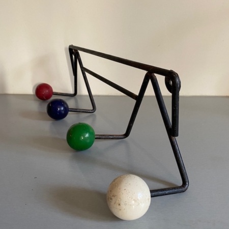 Le Porte-Manteaux Boules 1950, une structure métallique triangulaire vintage, accueille quatre boules colorées – rouge, bleue, verte et blanche – posées sur une surface grise. Brocante 93