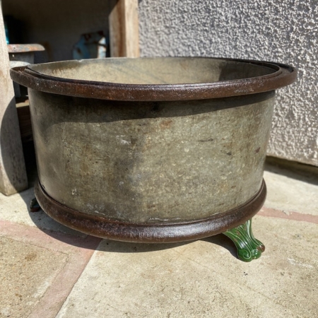 Le Fût Industriel 1940 VENDU, un grand pot rond en métal patiné au bord foncé, est placé sur une surface en béton où des zones ensoleillées et ombragées mettent en valeur son charme rétro et son attrait vintage, ce qui en fait une pièce remarquable. Brocante 93