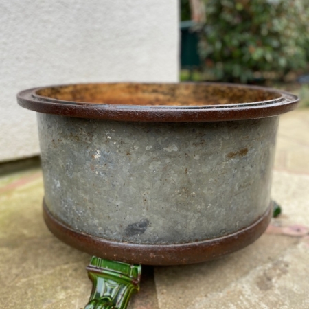 Jardinière rustique en métal "Fût Industriel 1940 VENDU" de forme ronde, patinée vieillie et pieds en céramique verte, dégageant un charme vintage alors qu'elle repose sur une surface en pierre. Brocante 93