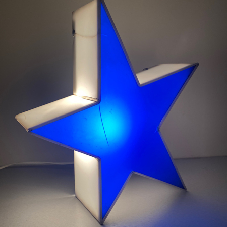 Une Étoile Lumineuse 1970 VENDU, présentant une forme d'étoile vintage avec des sections bleues et blanches, brille de mille feux dans une pièce faiblement éclairée. Brocante 93
