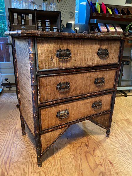 La Commode Bambou 1930 VENDU, une commode vintage en bois avec une finition vieillie et des poignées en laiton, ajoute un charme rétro à une pièce cosy avec parquet. Brocante 93