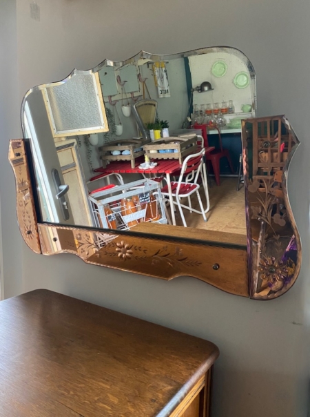 Un Miroir Bicolore 1950 VENDU reflète une cuisine chaleureuse avec des chaises rouges, une table en bois et des étagères ornées de contenants en verre. Brocante 93