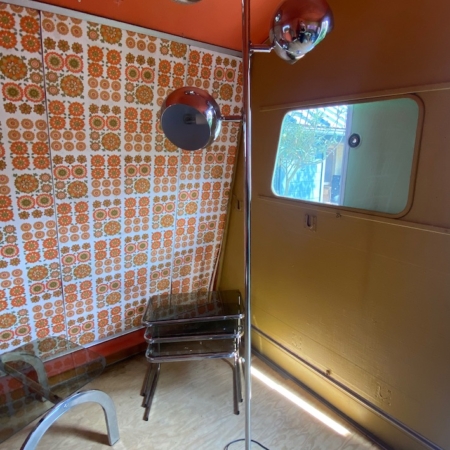 Le Lampadaire 1970 VENDU, un lampadaire vintage chromé à trois globes, trône dans une pièce rétro au papier peint fleuri orange et à la fenêtre verte. Brocante 93