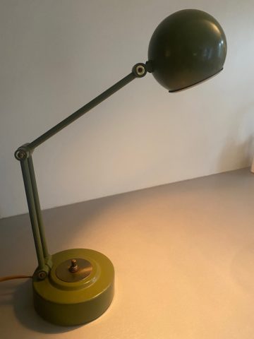 La Lampe de Bureau USA 1960, une lampe de bureau vintage verte réglable avec une base ronde et un abat-jour sphérique, est allumée et éclaire une partie de la surface. Brocante 93