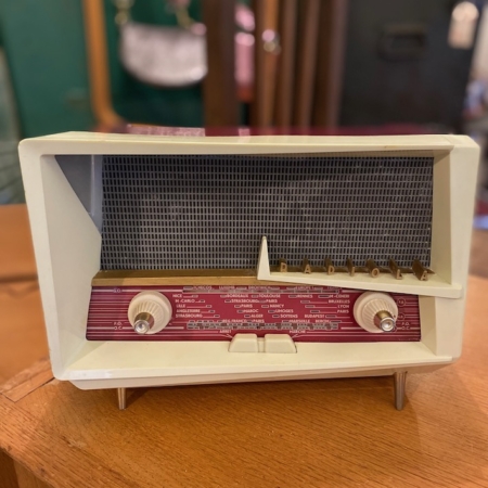 Une radio Bluetooth Radiola Le Corbusier de 1958 aux accents beiges et rouges, posée sur une surface en bois, sur un fond flou. Brocante 93