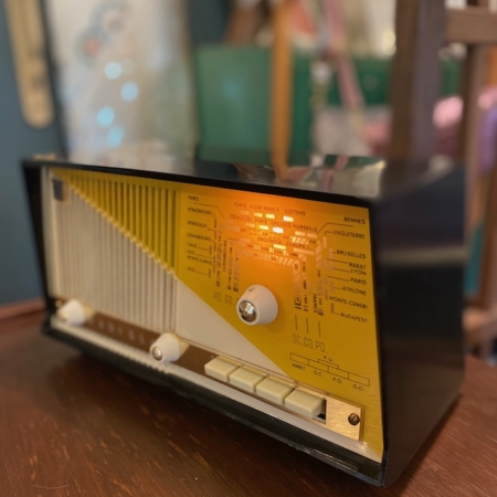 Une Radio TSF Radiola 1959 Bluetooth VENDU, avec ses cadrans et boutons lumineux en noir et jaune vintage, repose sur une surface en bois, évoquant une charmante ambiance rétro. Brocante 93