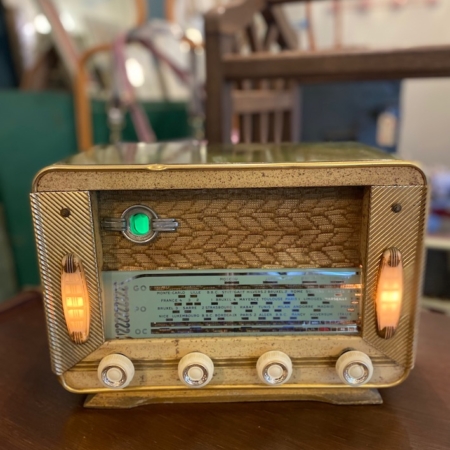 Une Radio TSF Réela 1957 VENDU avec cadrans et écran éclairés, posée sur une surface en bois, avec un arrière-plan flou. Brocante 93