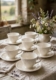 Cinq tasses à thé et soucoupes « Tasses à Thé » de la marque Wedgewood, blanches et gaufrées, posées sur une nappe en lin. Brocante 93