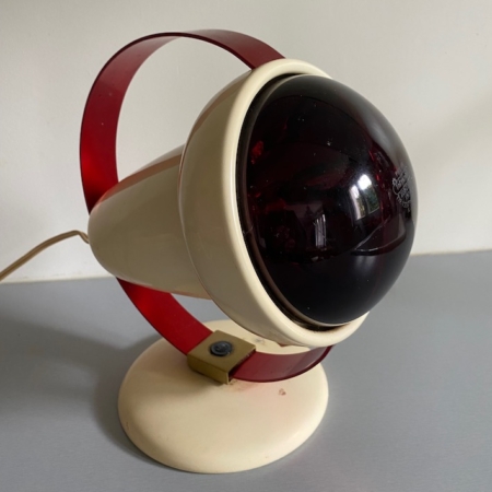 Voici la Lampe Charlotte Perriand 1960 VENDU, une charmante lampe de bureau vintage dotée d'une ampoule circulaire teintée de rouge associée à une base sphérique blanche, élégamment posée sur une surface grise. Idéale pour insuffler à votre espace ce charme caractéristique du brocante 93. Brocante 93