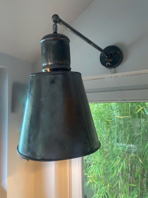 Une applique Applique Industrielle 1960 en noir est suspendue à côté d'une fenêtre, avec des bambous verts visibles à l'extérieur. Brocante 93