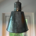 Une grande suspension Applique Industrielle 1960 en métal est suspendue devant une fenêtre avec de la verdure à l'extérieur, capturant le charme vintage de son design de 1960. Brocante 93