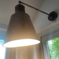 L'Applique Industrielle 1960 est une lampe murale en métal avec un abat-jour conique, idéale près des fenêtres et des murs blancs, évoquant une esthétique caractéristique des années 1960. Brocante 93