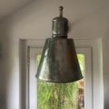 L'Applique Industrielle 1960, une lampe suspendue métallique de style industriel, est suspendue devant une fenêtre avec des bambous à l'extérieur. Brocante 93