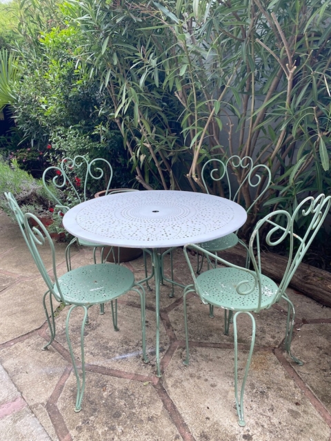 Le Salon de jardin en fer forgé 1960, une table de patio ronde en métal vintage avec quatre chaises assorties, apporte une ambiance extérieure charmante lorsqu'elle est placée à proximité de plantes à feuilles vertes. Brocante 93