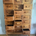 Le Meuble de métier en bois 1940, pièce vintage, met en valeur ses multiples tiroirs légèrement entrouvertes alors qu'il repose sur un plancher en bois. Brocante 93