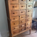 Ce meuble en bois vintage "Meuble de métier en bois 1940" comporte plusieurs petits tiroirs et des pieds angulaires. Brocante 93