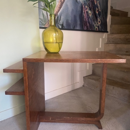 Une Desserte à plateaux 1940, de style meuble vintage, abrite un vase jaune avec des lys blancs à côté des escaliers et un art mural de paon accrocheur. Brocante 93