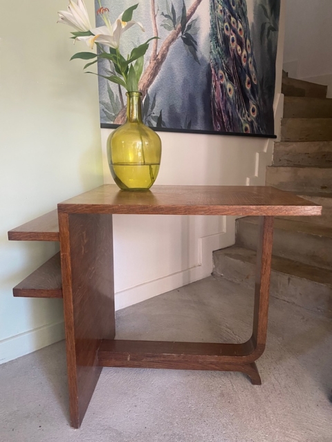 Une Desserte à plateaux 1940, de style meuble vintage, abrite un vase jaune avec des lys blancs à côté des escaliers et un art mural de paon accrocheur. Brocante 93