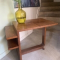 Table d'appoint Desserte à plateaux 1940 en bois avec un vase en verre vert et des fleurs blanches, placée à côté d'un escalier et d'un tableau de paon. Brocante 93