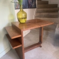 Une table d'appoint Desserte à plateaux 1940 avec un vase jaune de lys blancs se trouve à côté des escaliers et des œuvres d'art murales. Brocante 93