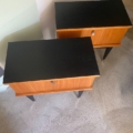 La "Paire de tables de nuit 1950" aux plateaux noirs et aux pieds inclinés est présentée sur un sol en béton près des escaliers. Brocante 93