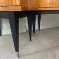 Des pieds de meubles fuselés noirs avec des embouts en métal inspirés des années 1950 reposent sur un sol gris lisse, soutenant des armoires en bois et la Paire de tables de nuit 1950. Brocante 93