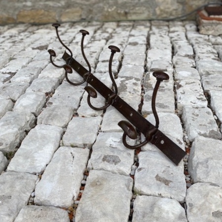 La Porte-Manteaux industrielle 1950, dotée de crochets métalliques, se dresse sur un sol pavé de pierres, à côté d'un solide mur de pierre. Brocante 93
