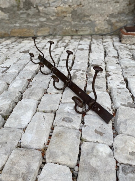 La Porte-Manteaux industrielle 1950, dotée de crochets métalliques, se dresse sur un sol pavé de pierres, à côté d'un solide mur de pierre. Brocante 93