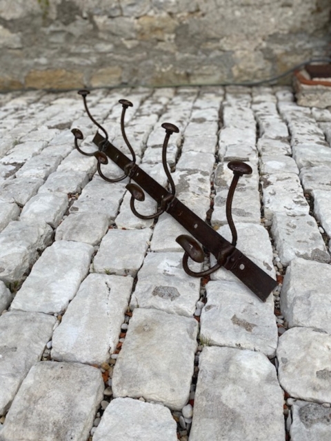 La Porte-Manteaux industrielle 1950, dotée de crochets métalliques, se dresse sur un sol pavé de pierres, à côté d'un solide mur de pierre. Brocante 93