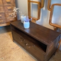 Meuble industriel en métal riveté, un banc en bois foncé avec deux tiroirs, décoré de vases de fleurs séchées à côté d'étagères murales modernes en bois. Brocante 93