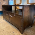 Le Meuble industriel métal riveté est une armoire en bois foncé avec deux portes et une étagère ouverte, présentant des accents métalliques rivetés pour un look industriel authentique, placée sur un plancher en bois à côté d'autres meubles. Brocante 93