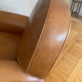 Gros plan d'un fauteuil Paire de fauteuils Club 1940 en cuir marron, présentant des coutures apparentes avec un plancher en bois en arrière-plan. Brocante 93