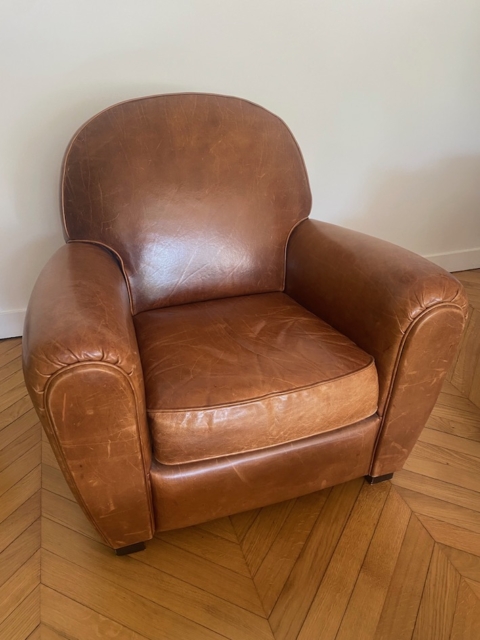 Une paire de fauteuils Club 1940 en cuir marron classique repose sur un parquet en bois contre un mur blanc uni. Brocante 93