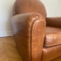 Gros plan de la Paire de fauteuils Club 1940, fauteuils vintage en cuir marron sur un plancher en bois contre un mur blanc. Brocante 93
